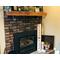 This shows the rustic location sign decorating a fireplace hearth. The wood sign is rectangular in shape and leans against the brick.